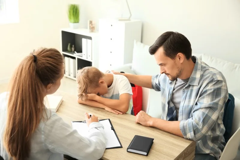 Parent comforting child at desk with professional