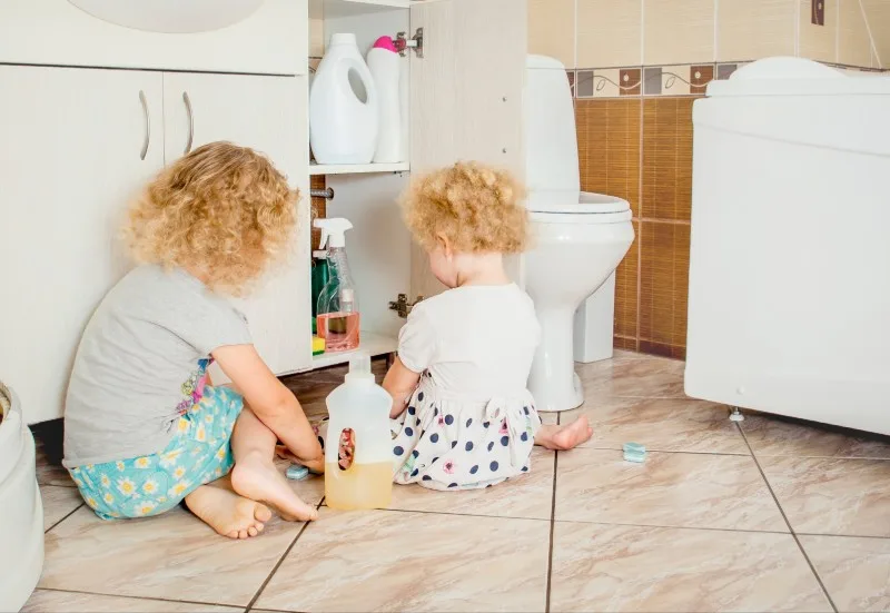 Two toddlers sitting on bathroom floor playing with bottles
