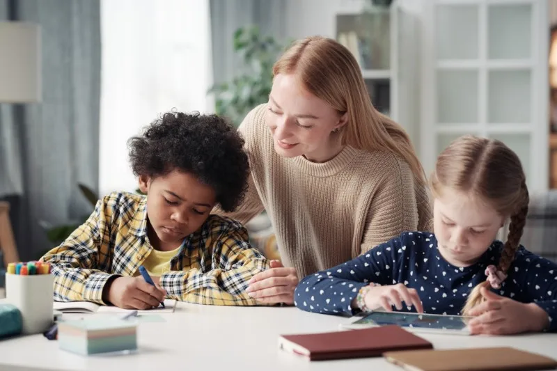 Teacher assisting two children at table