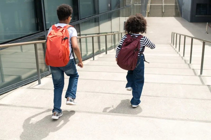Two children with backpacks walking up outdoor stairs