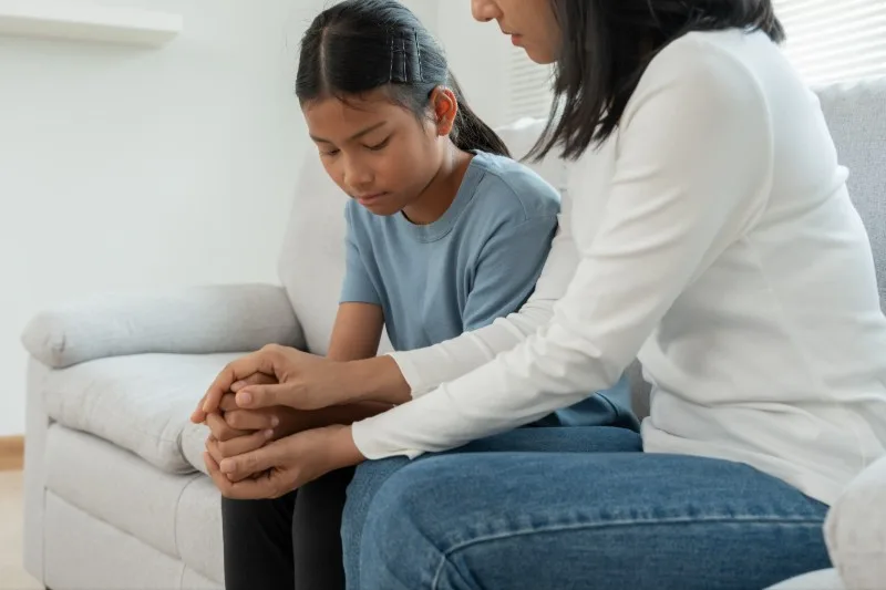 Adult comforting seated child on couch