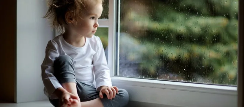 Young child sitting on windowsill looking outside