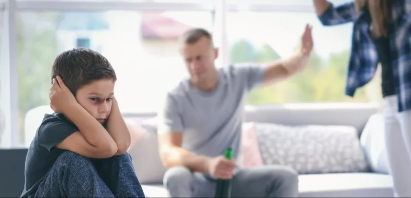 Child covering ears on couch while adults argue