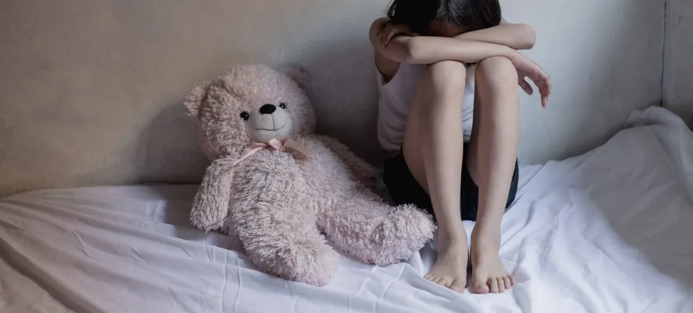 Child sitting on bed with large teddy bear