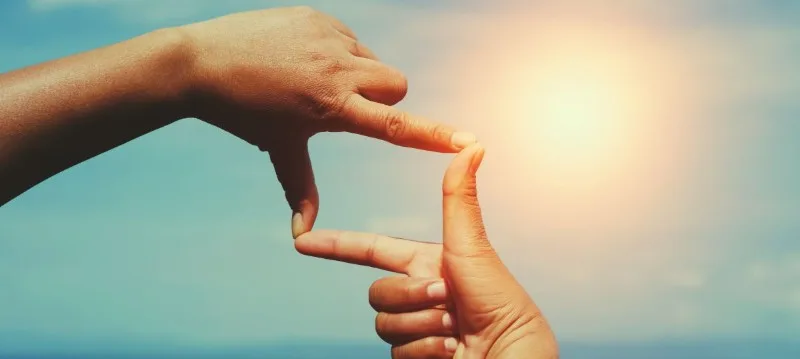 Hands framing sun over sky