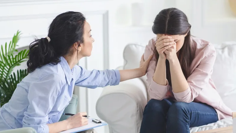 Woman comforting another woman covering her face