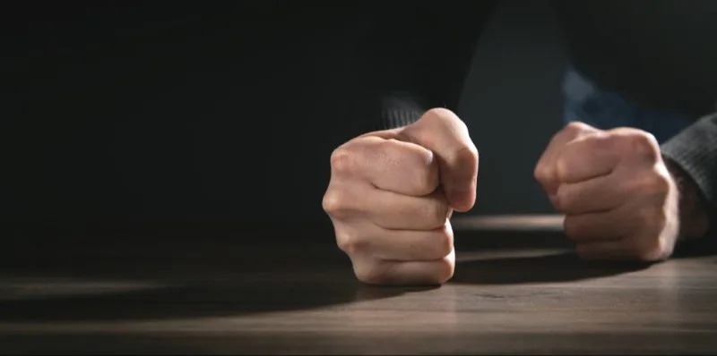 Clenched fists resting on wooden table