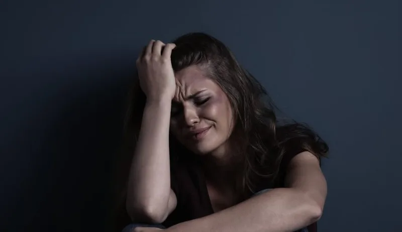 Woman sitting and holding her head with eyes closed