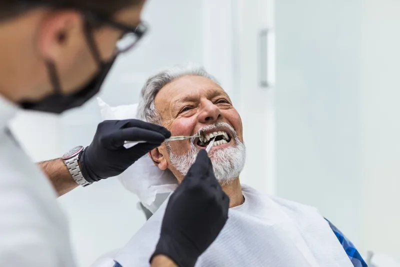 Senior man receiving dental exam from masked clinician