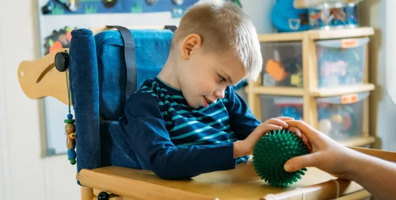 Young boy in chair reaching for textured sensory ball