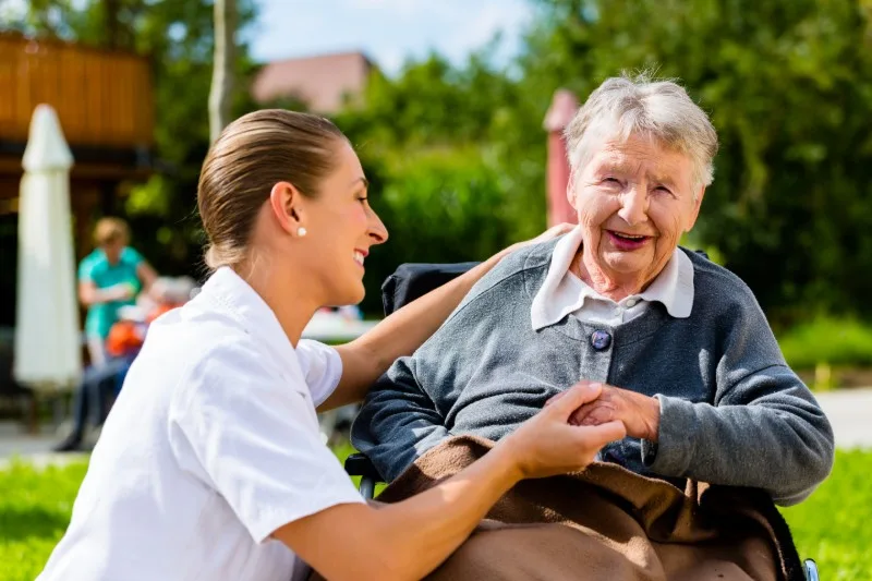 Care worker holding hands with elderly woman outdoors