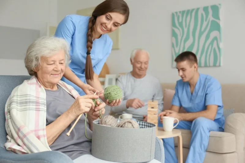 Care worker helping an older woman with knitting in a lounge