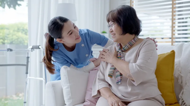 Caregiver assisting older woman on couch