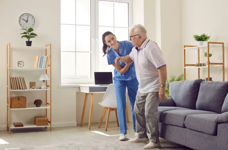 Care worker assisting elderly man to stand