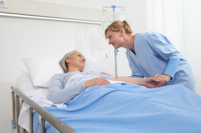 Caregiver holding patient's hand at bedside