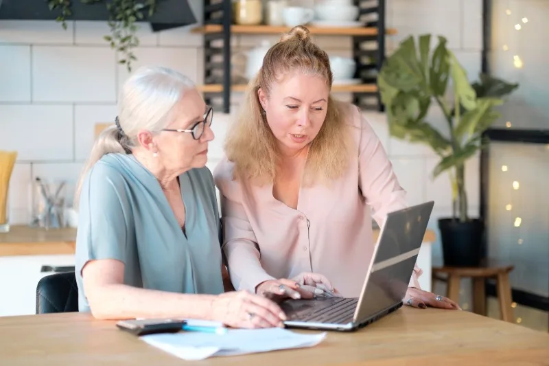 Two women using a laptop at a kitchen table