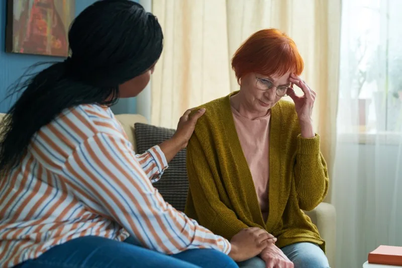 Caregiver comforting older woman on couch