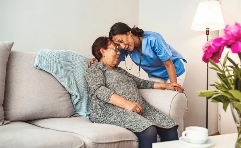 Younger female caregiver leaning toward older woman on sofa
