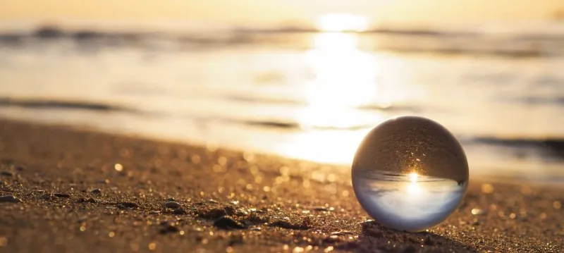 Glass sphere on sandy beach at sunset