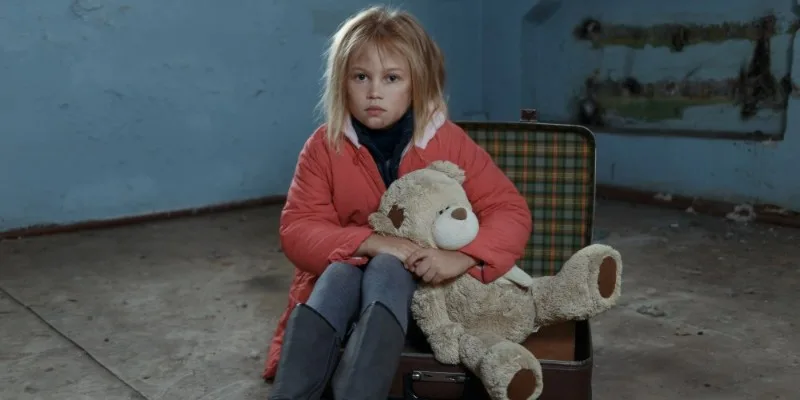 Young girl sitting on suitcase holding stuffed bear