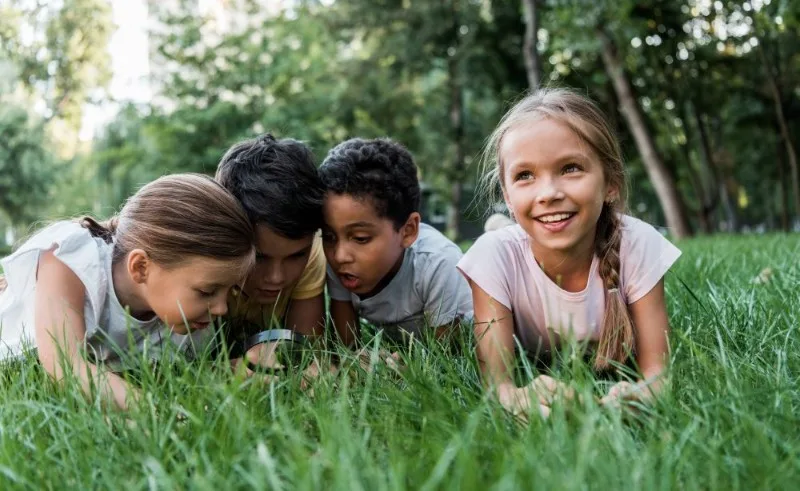 Four children lying on grass looking at a phone