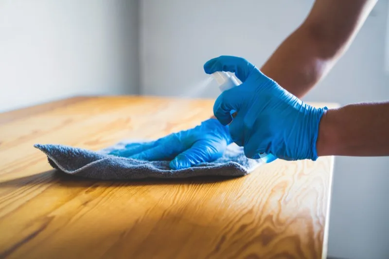 Person wiping wooden table with blue glove