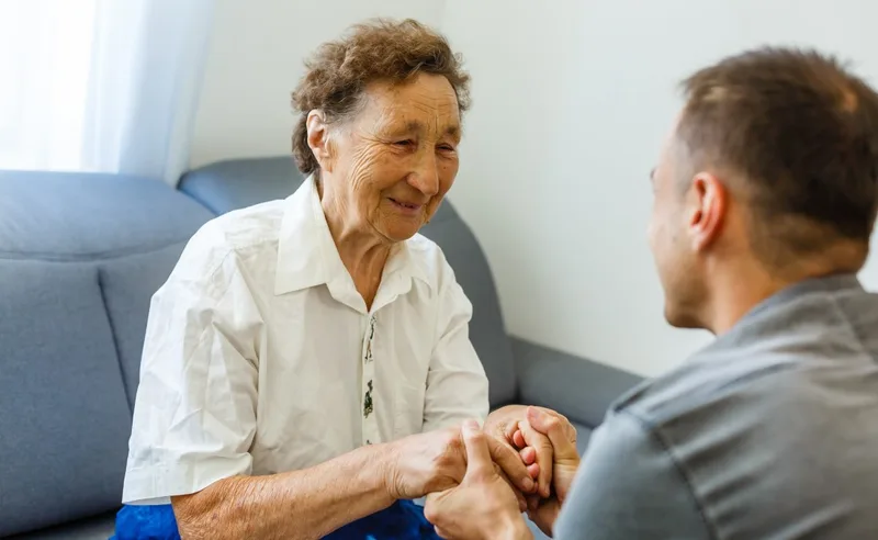 Elderly woman holding younger man's hands