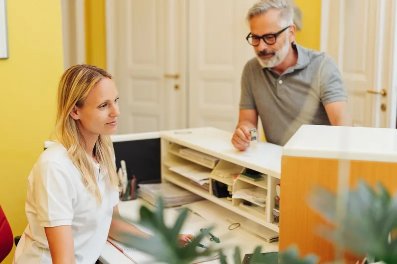 Female dental receptionist at front desk speaking with male patient