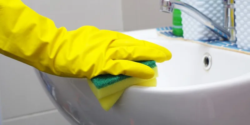 Hand in yellow glove wiping white bathroom sink