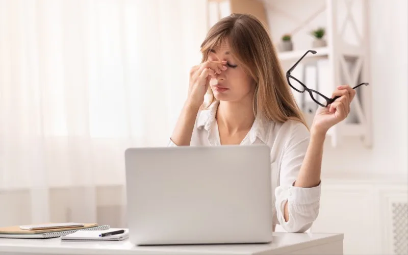 Person rubbing eyes while using laptop