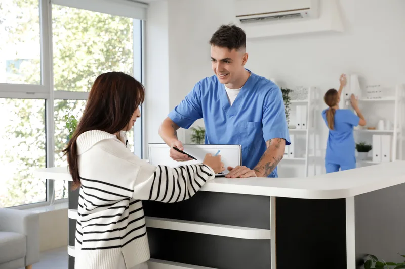 Reception staff working with a female patient at a clinic desk