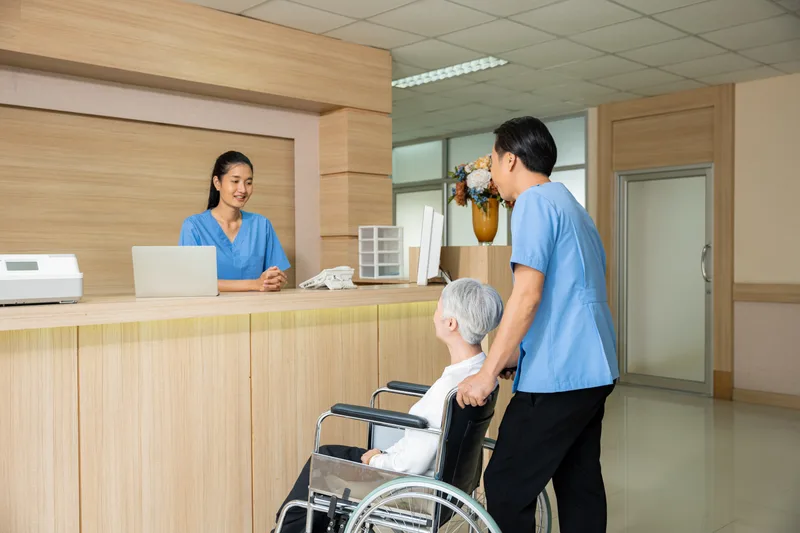 Elderly patient in a wheelchair speaking with reception staff