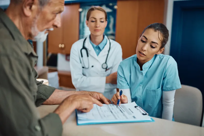 Nurse assisting a senior man with medical documents at reception