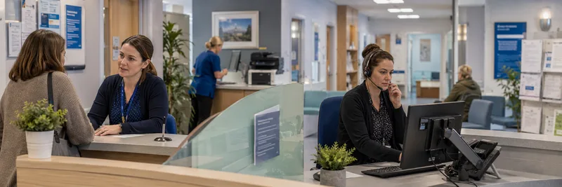 GP practice reception desk with staff and patients