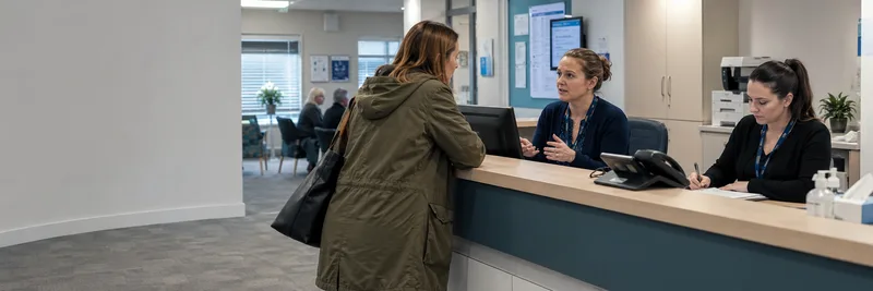 GP practice reception desk with staff and patient