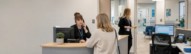 GP reception desk with receptionist speaking to patient