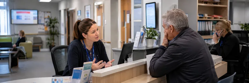 Receptionist speaking with older male patient at desk