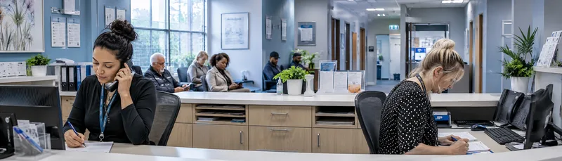 Two GP receptionists working at busy desk