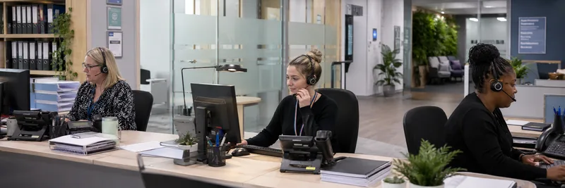 Three reception staff at desk using phones and computers