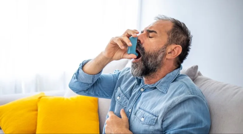 Adult man using blue inhaler while seated