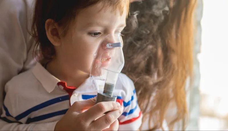 Child holding a nebulizer mask to face