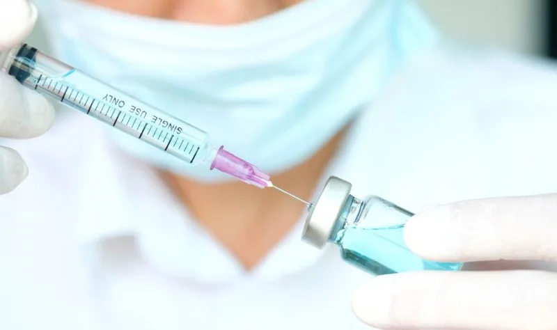 Gloved hands drawing vaccine from vial with syringe