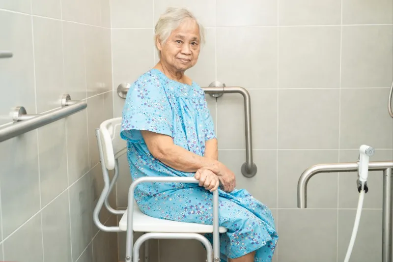 Older person seated on a shower chair in an accessible bathroom