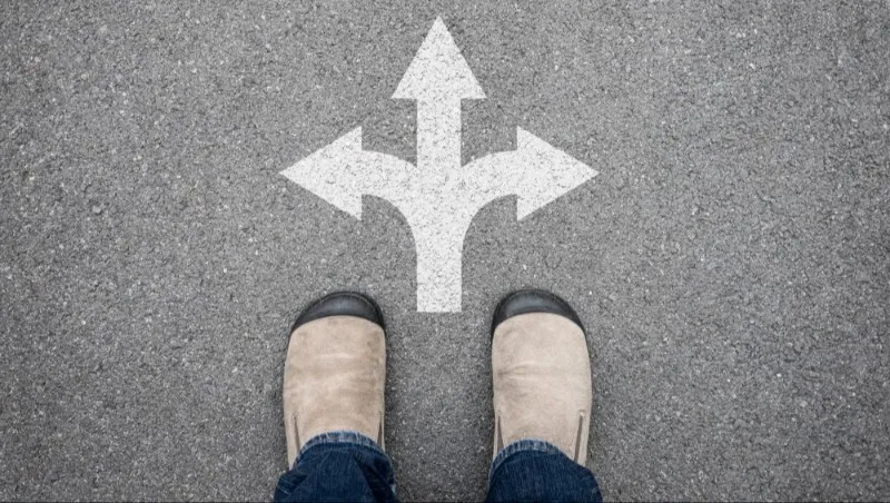 Shoes standing before three-way directional arrow on pavement