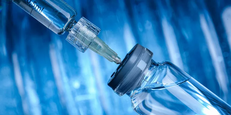 Syringe drawing fluid from vaccine vial