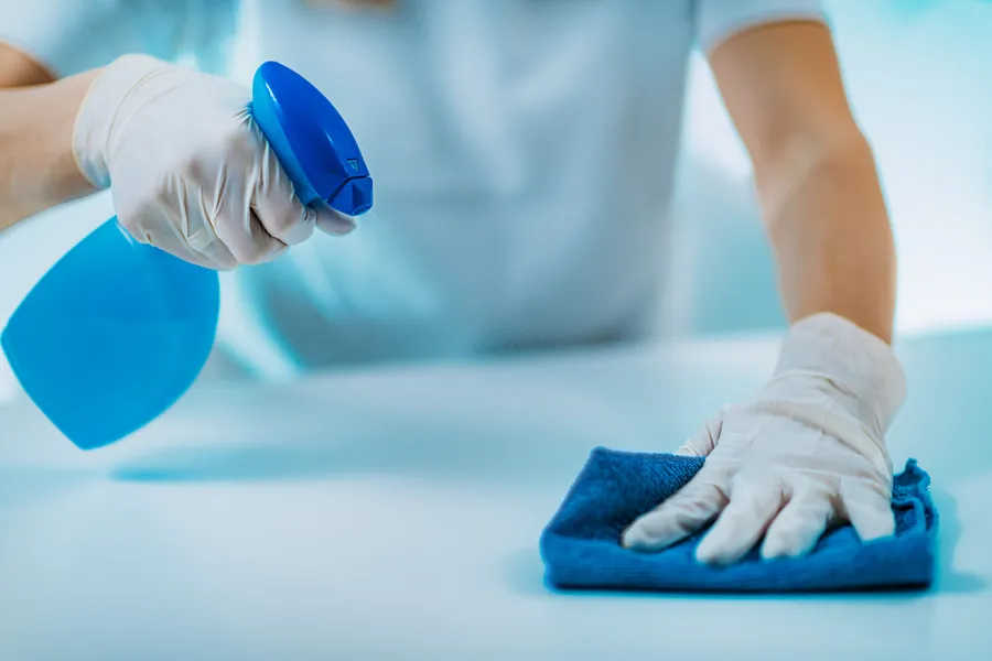 Gloved hands spraying and wiping a surface