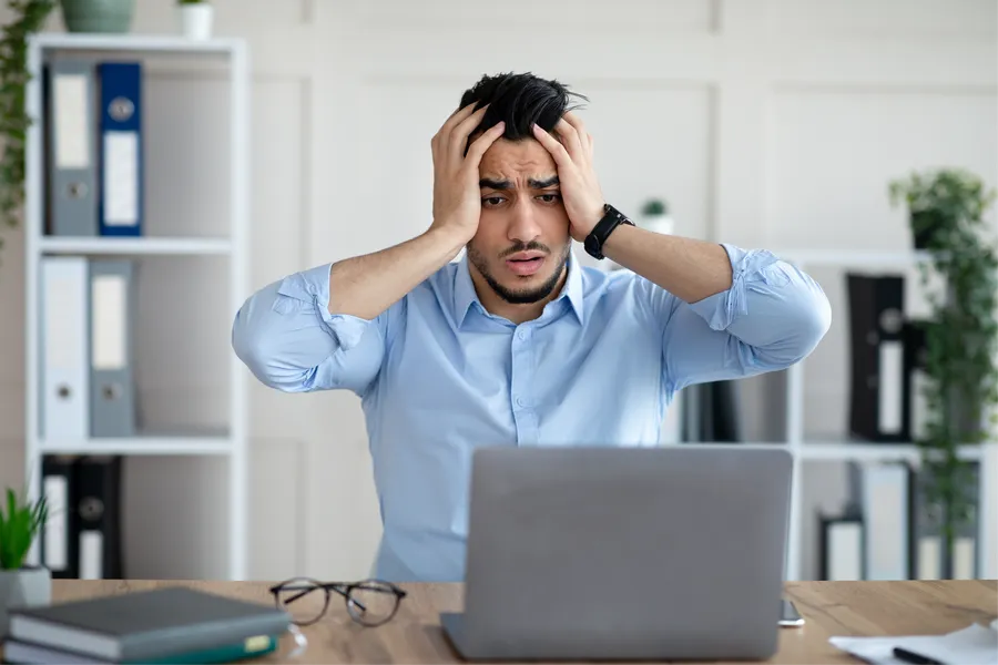 Man at desk holding head with hands