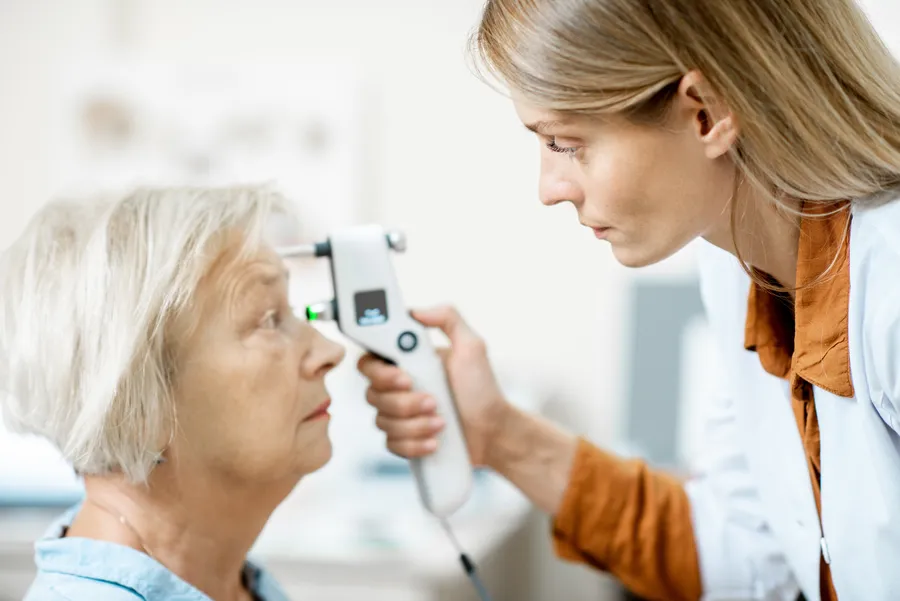 Woman examining older woman's eye with handheld device