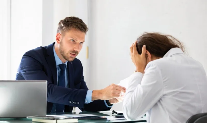 Manager pointing at seated employee holding head