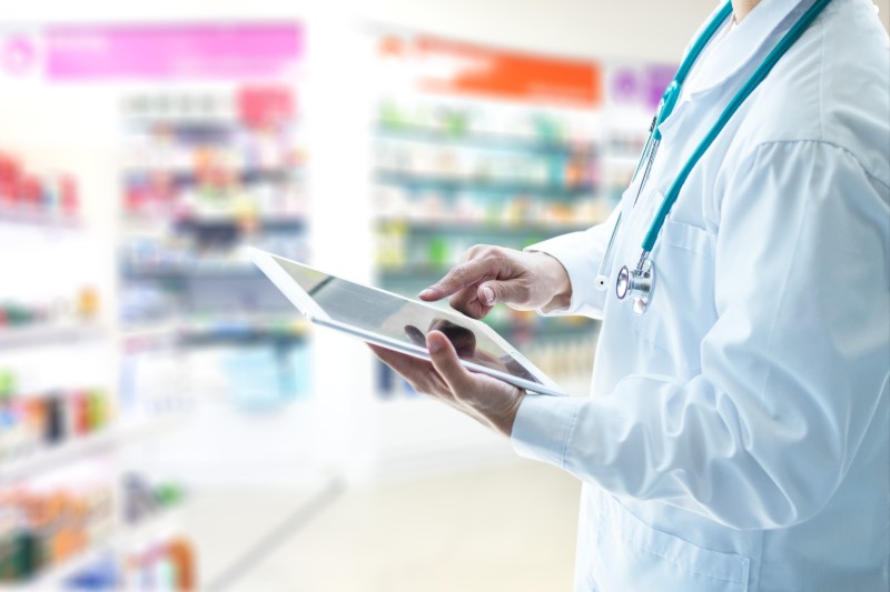 Person in lab coat using tablet in pharmacy